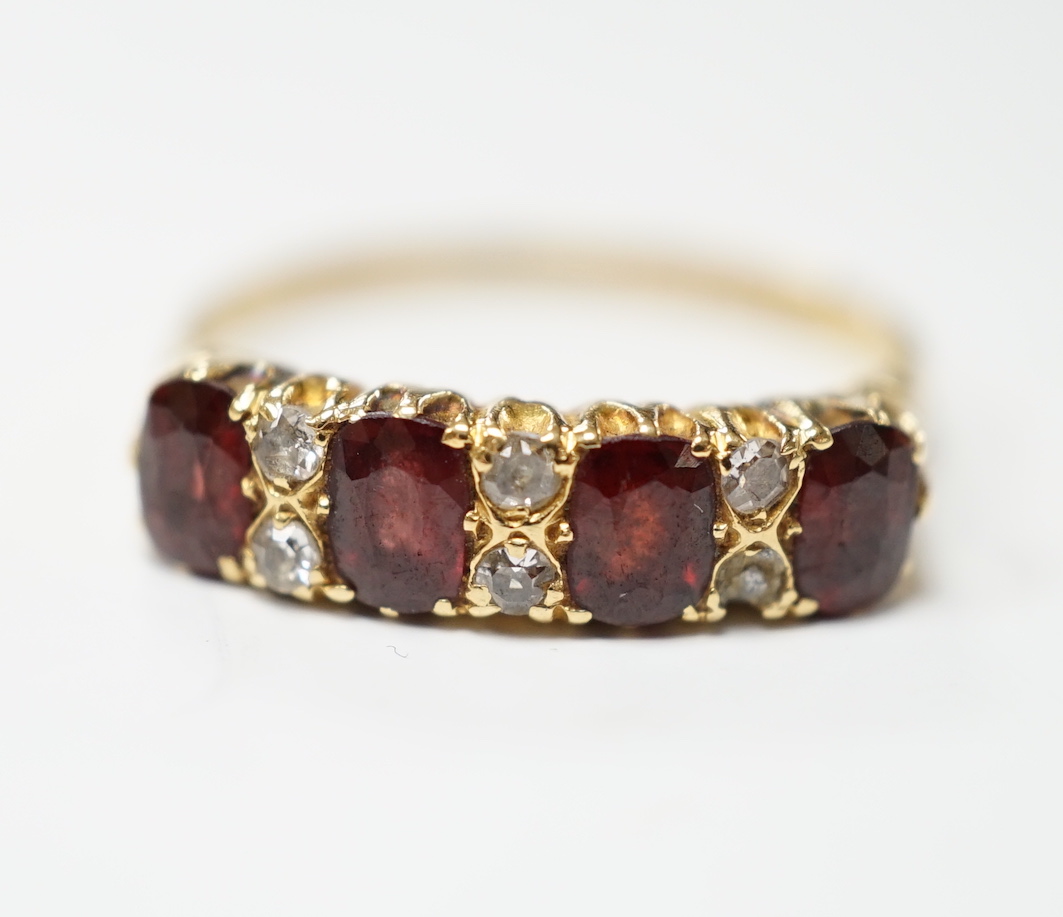 An Edwardian 18ct gold and four stone garnet set half hoop ring, with diamond chip spacers, size R, gross weight 3.6 grams.